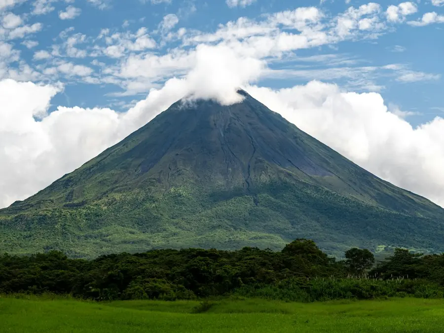 Arenal Volcano rising above green pastures under a cap of cloud
